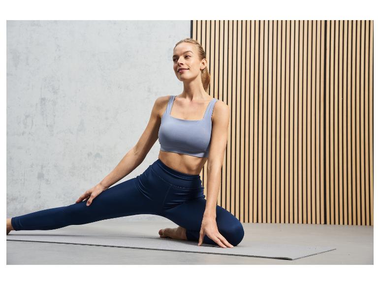 Eine Frau in einem blauen Sport-BH und Leggings macht Yoga auf einer grauen Matte.