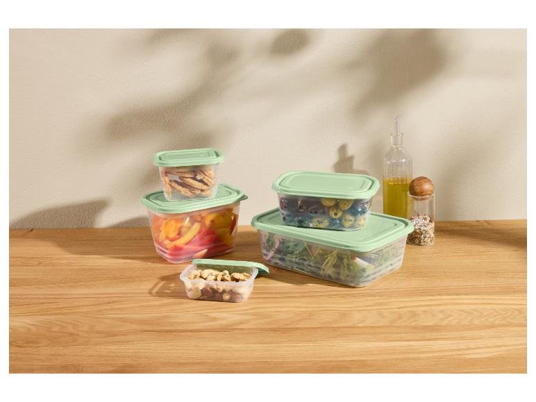 Plastikbehälter mit grünen Deckeln, gefüllt mit Gemüse, Nüssen und Crackern auf einem Holztisch.