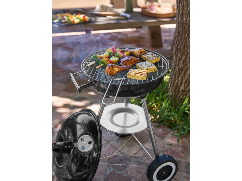 Holzkohlegrill mit Hähnchen, Halloumi und Gemüsespießen, die draußen garen.