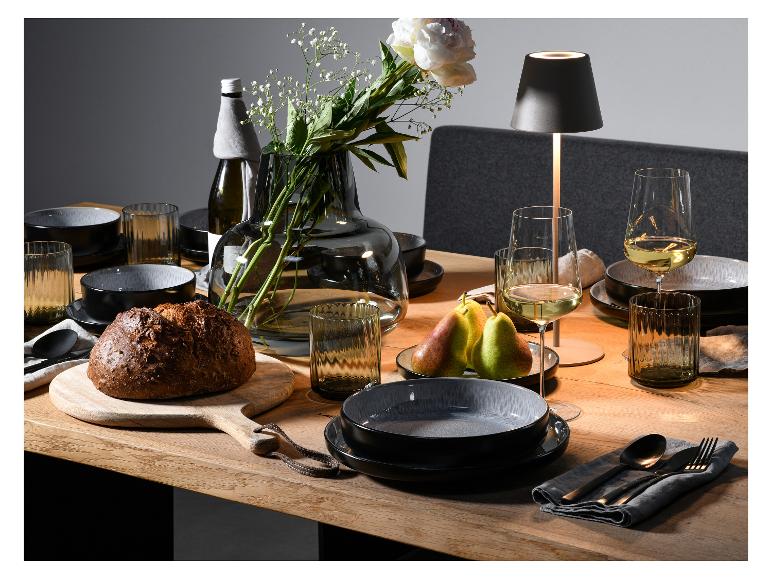 Ein gedeckter Tisch mit schwarzem Geschirr, Gläsern und Besteck.