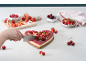 Herzförmiger Kuchen mit Früchten, angeschnitten, umgeben von Erdbeeren, Himbeeren und Kirschen.