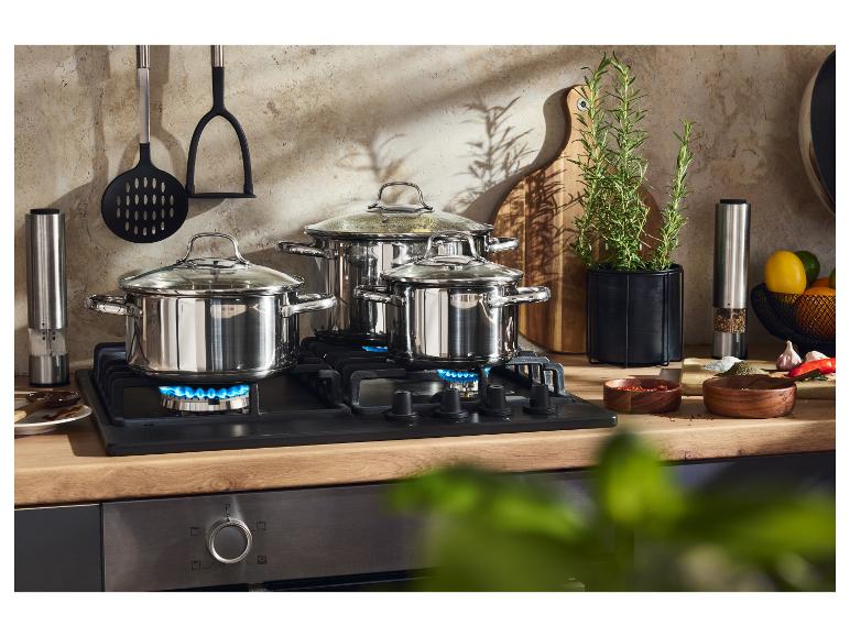 Drei Edelstahltöpfe auf einem Gasherd, mit Küchenutensilien und Kräutern