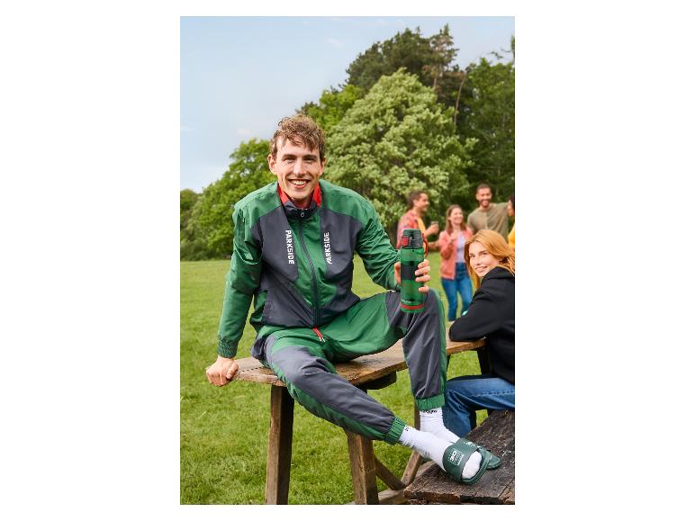 Lächelnder Mann in einer grün-grauen PARKSIDE® Jacke sitzt im Freien.