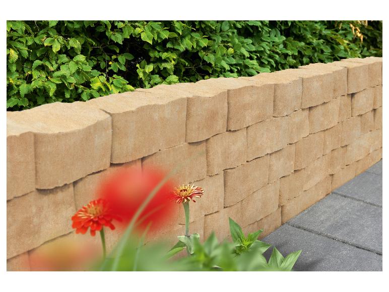 Stützmauer aus beigen Betonsteinen mit grünen Pflanzen und roten Blumen.