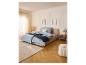 Schlafzimmer mit Bett, LIVARNO® Nachttisch, Teppich und Pouf in hellen Farben.