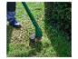 Person trimmt Rasen mit einem Rasentrimmer neben einer Hecke.