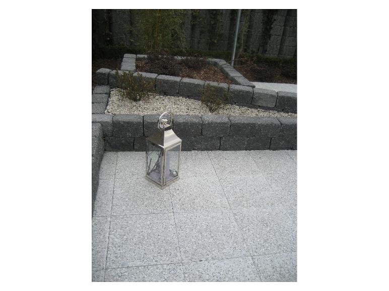 Silberne Laterne auf einer Terrasse mit grauen Fliesen und einem Hochbeet.