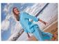 Frau in hellblauem Leinenhemd und Hose am Strand, blickt nach oben.