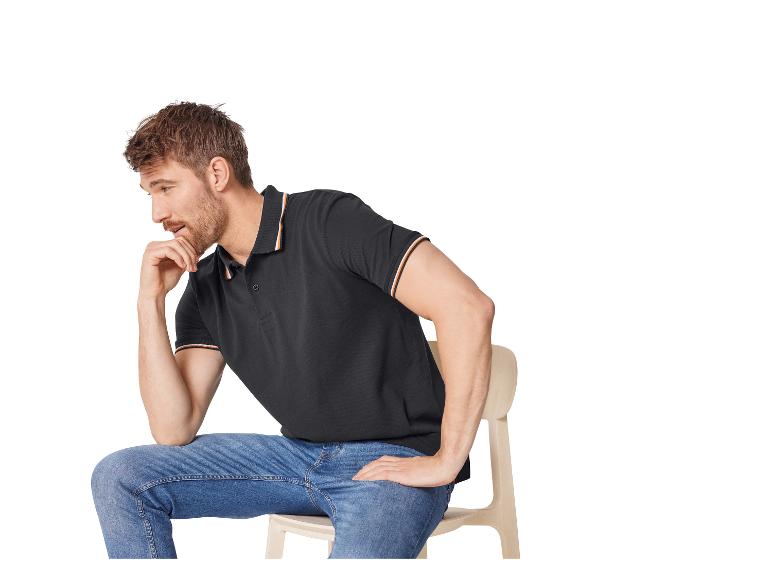 Ein nachdenklicher Mann in einem schwarzen Poloshirt und Jeans sitzt auf einem Stuhl.