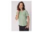 Frau in hellgrünem T-Shirt und schwarzer Hose, mit Hand in der Tasche.