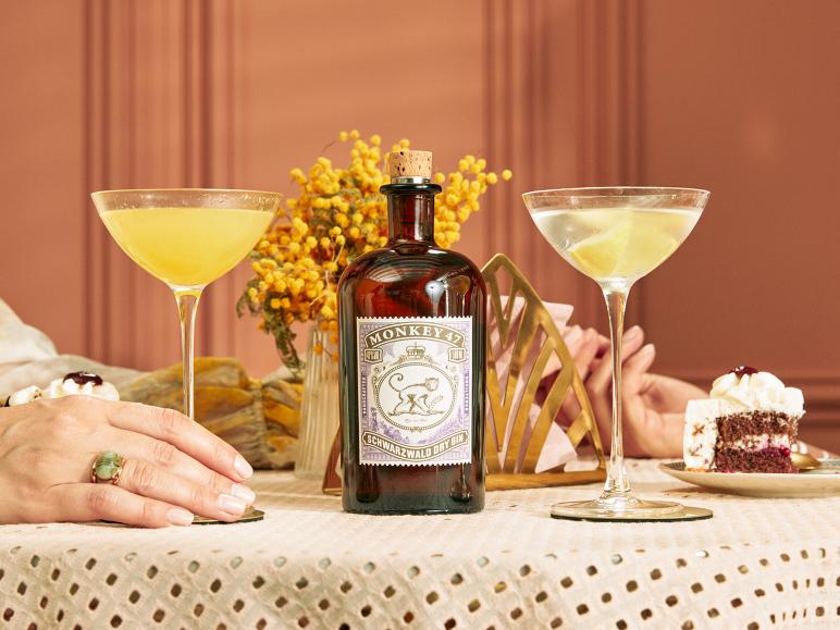 Gin-Flasche, zwei Cocktails und Kuchen auf einem Tisch mit den Händen einer Person.