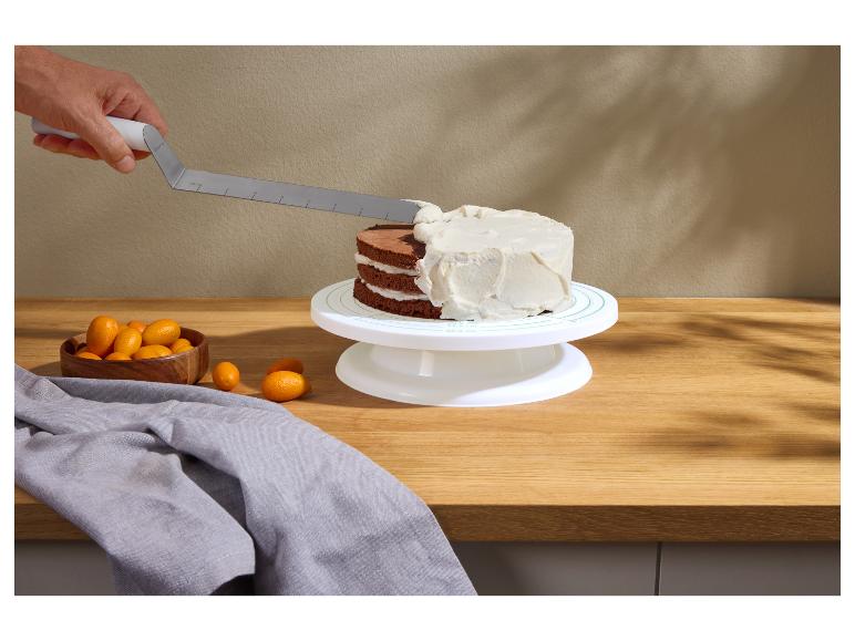 Hand glasiert eine Schokoladentorte auf einem Drehteller, mit Kumquats und einem grauen Tuch daneben.