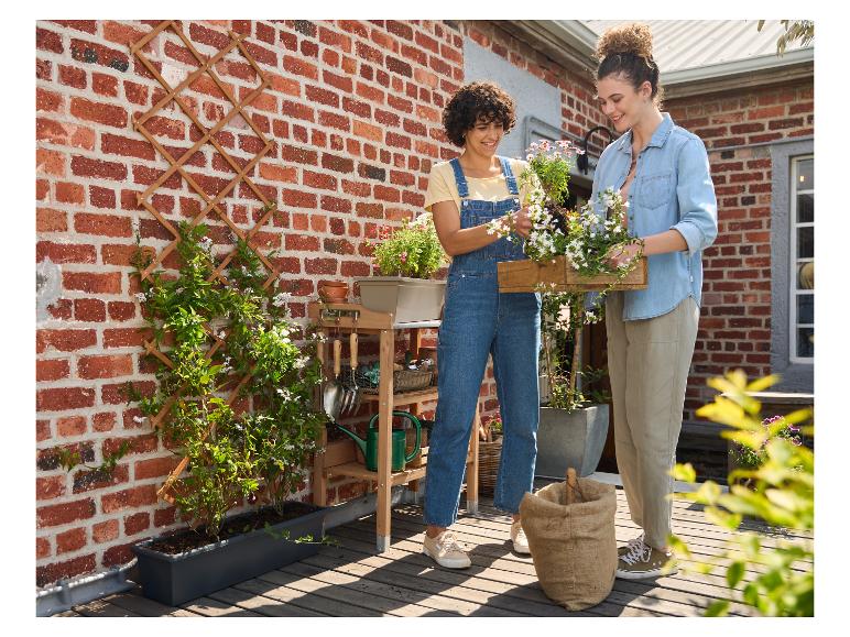 Zwei Frauen pflanzen Blumen in einen Blumenkasten auf einer Holzterrasse.
