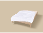 Einzelbett mit weißer Bettdecke und beigem Laken auf neutralem Hintergrund.