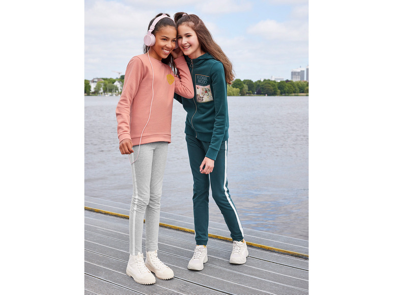 Zwei Mädchen in lässiger Kleidung mit einem rosafarbenen Pullover und einem grünen Hoodie mit weißen Streifen.