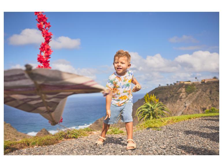 Junge in Dinosaurier-T-Shirt und Shorts spielt an der Küste.