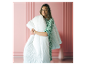 Lächelnde Frau hält eine weiße Bettdecke, trägt ein grünes Kleid mit Blumenmuster.