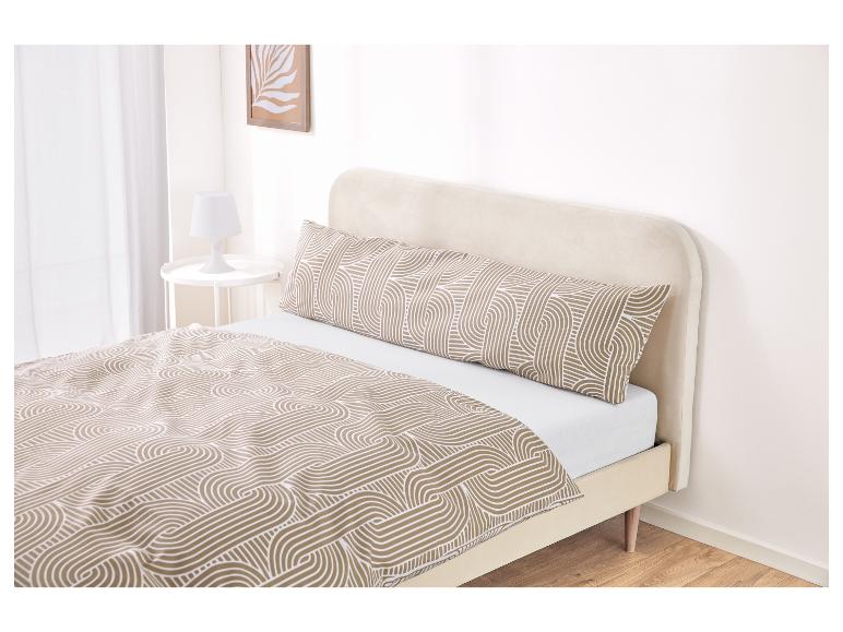 Ein Bett mit beigem Kopfteil und gemusterter Bettdecke und Seitenschläferkissen.