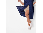 Frau in marineblauem Hemdblusenkleid und beigefarbenen Shorts, weiße Sneaker.
