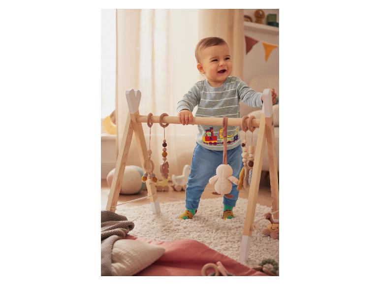 Ein Baby spielt mit einem Holzspielbogen mit verschiedenen Spielzeugen.