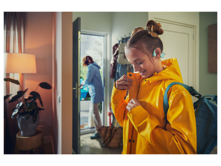Ein Mädchen in einem gelben Regenmantel mit Rucksack trägt Kopfhörer.