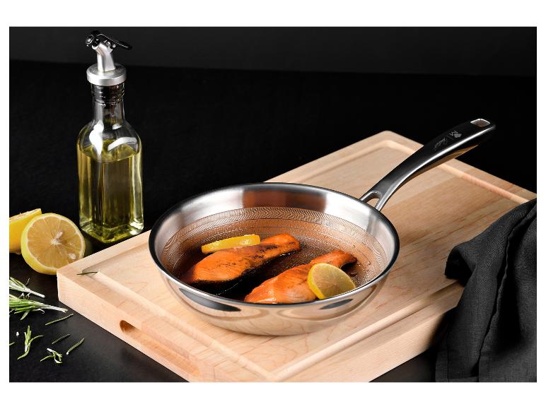 Edelstahlpfanne mit Lachs und Zitrone auf einem Holzschneidebrett.