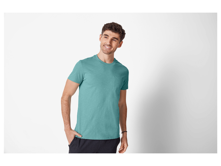 Ein lächelnder Mann trägt ein türkisfarbenes T-Shirt mit Tasche.