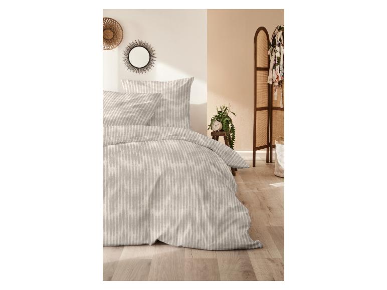 Graue Bettwäsche mit Muster und passenden Kissen in einem hellen Schlafzimmer.