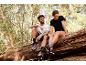 Zwei Personen in Sportkleidung sitzen auf einem Baumstamm im Wald.