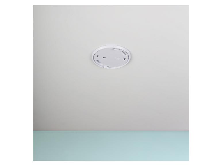 Eine weiße Rauchmelderbasis ist an einer weißen Decke über einer hellblauen Wand montiert.