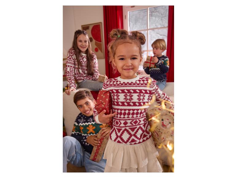 Vier Kinder in festlichen Weihnachtspullovern, die verpackte Geschenke halten.
