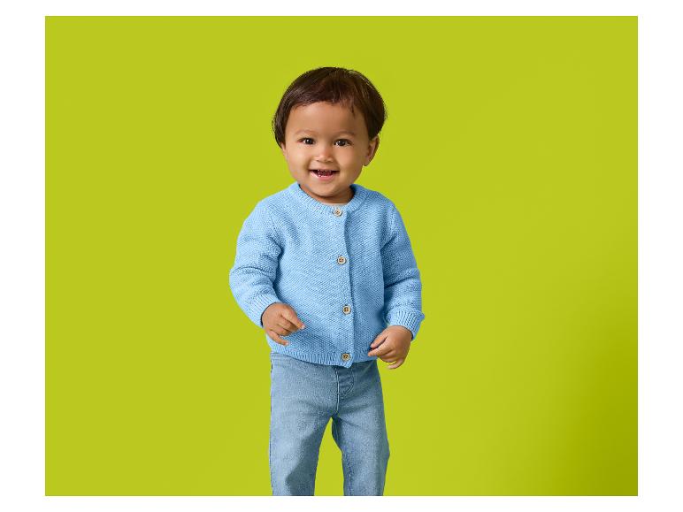 Lächelndes Baby in blauem Strickcardigan und Jeans.