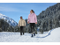 Paar in Winterjacken und Hosen, das auf einem verschneiten Bergpfad wandert.