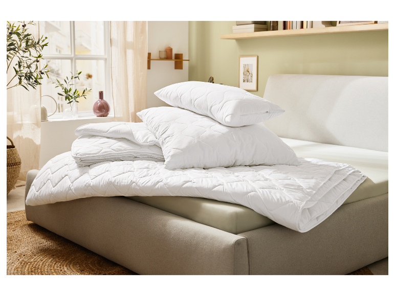 Weiße, gesteppte Kissen und Bettdecke auf einem Bett.