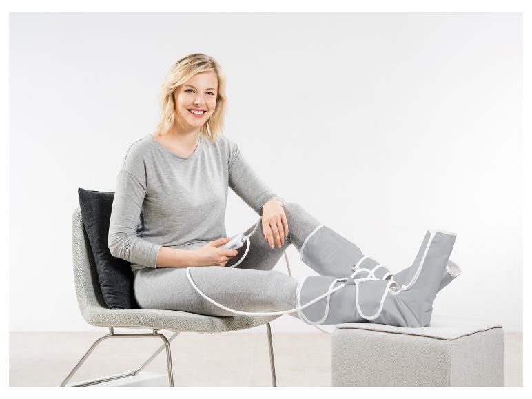 Frau sitzt auf einem Stuhl mit Beinmassagegerät und lächelt.