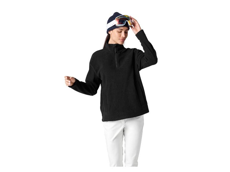 Frau in schwarzem Fleece-Pullover, weißer Hose und Skibrille auf Mütze.