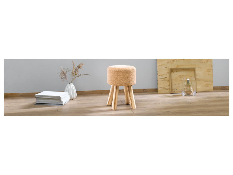 Ein beigefarbener Plüschhocker auf Holzbeinen in einem modernen Interieur.