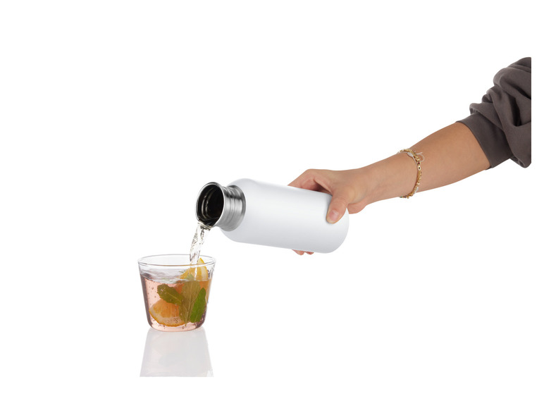 Eine Hand gießt Wasser aus einer weißen Thermosflasche in ein Glas mit Zitrone und Minze.