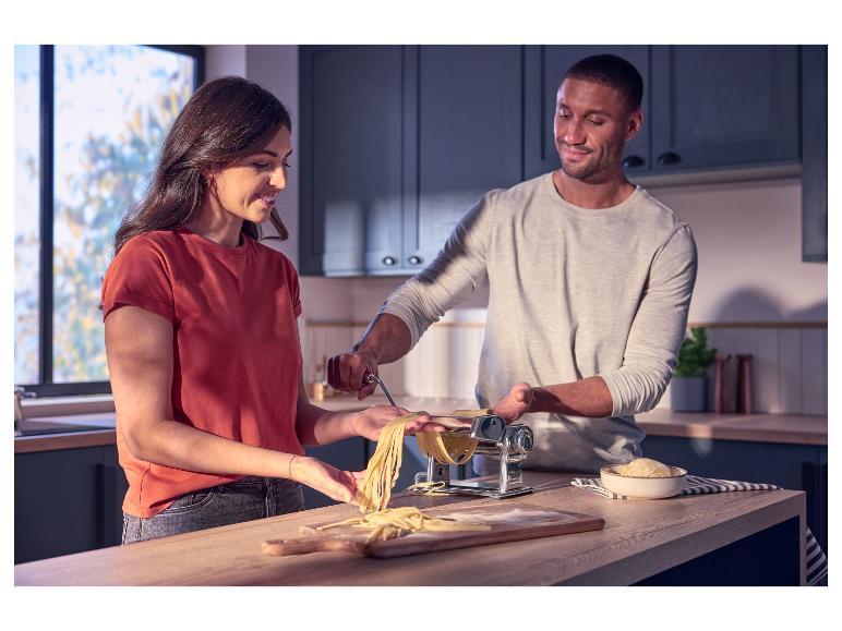 Paar macht frische Pasta mit Nudelmaschine in moderner Küche.