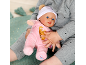 Ein Kind hält eine Baby-Puppe in einem rosa Strampler und einer weißen Mütze.