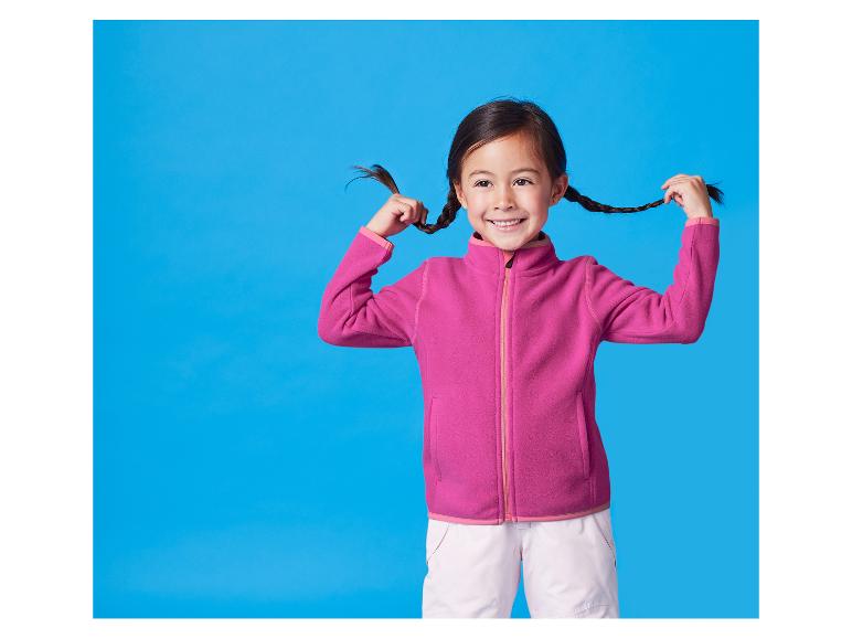 Ein lächelndes Mädchen in einer pinken Fleecejacke hält ihre Zöpfe.