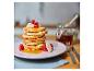 Stapel Pfannkuchen mit Banane, Himbeeren und Honig auf einem rosa Teller.