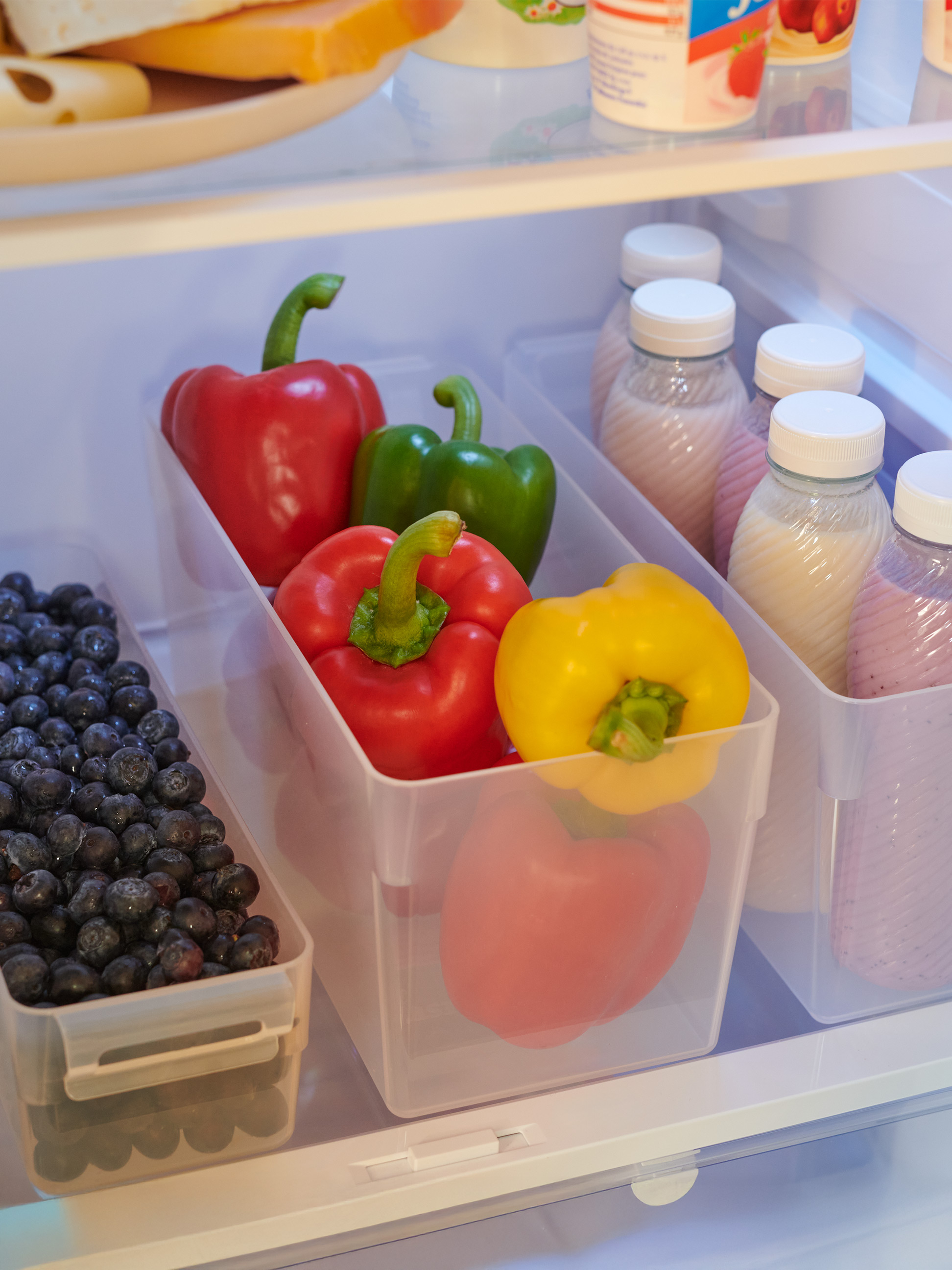 Bunte Paprika und Heidelbeeren in transparenten Behältern in einem organisierten Kühlschrank.