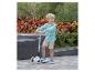Blonder Junge in kariertem Hemd und beigen Shorts, steht auf einem dreirädrigen Roller.