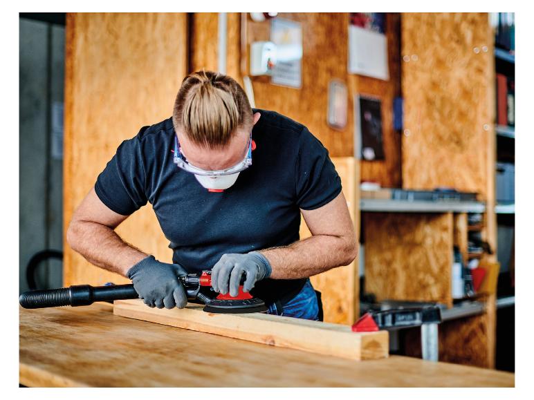 Mann schleift Holz mit einem Exzenterschleifer, trägt Schutzbrille und Handschuhe.