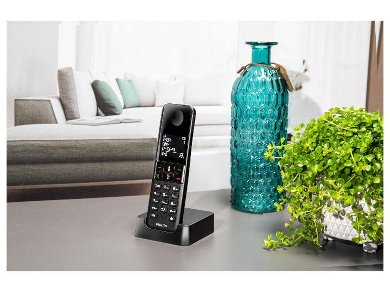 Schnurloses Telefon mit Ladestation auf einem Tisch, neben einer Vase und Pflanze.