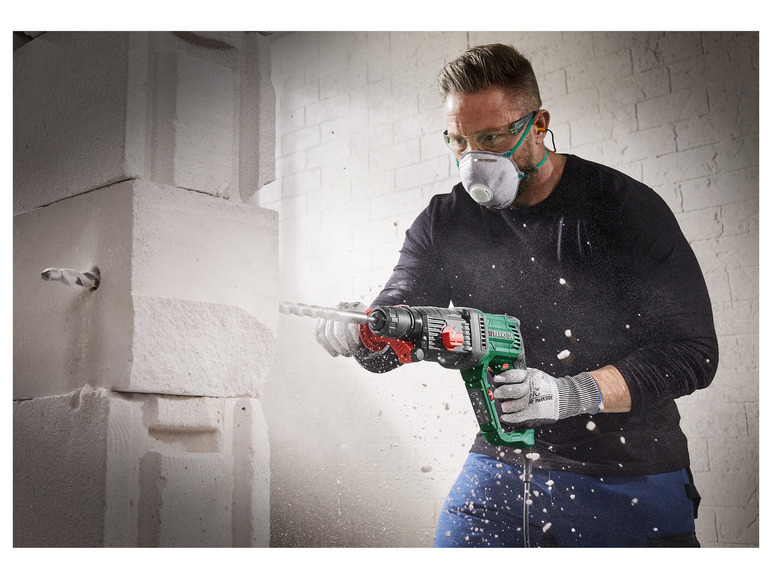 Ein Mann bohrt mit einem Parkside Bohrhammer in eine Wand.