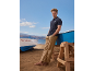 Mann in marineblauem Poloshirt und beiger Hose am Strand mit Booten.