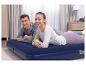 Lächelndes Paar entspannt auf einer Bestway Luftmatratze im Schlafzimmer.