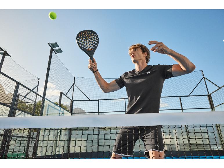 Mann spielt Padel, hält einen Padelschläger, mit einem Tennisball in der Luft.
